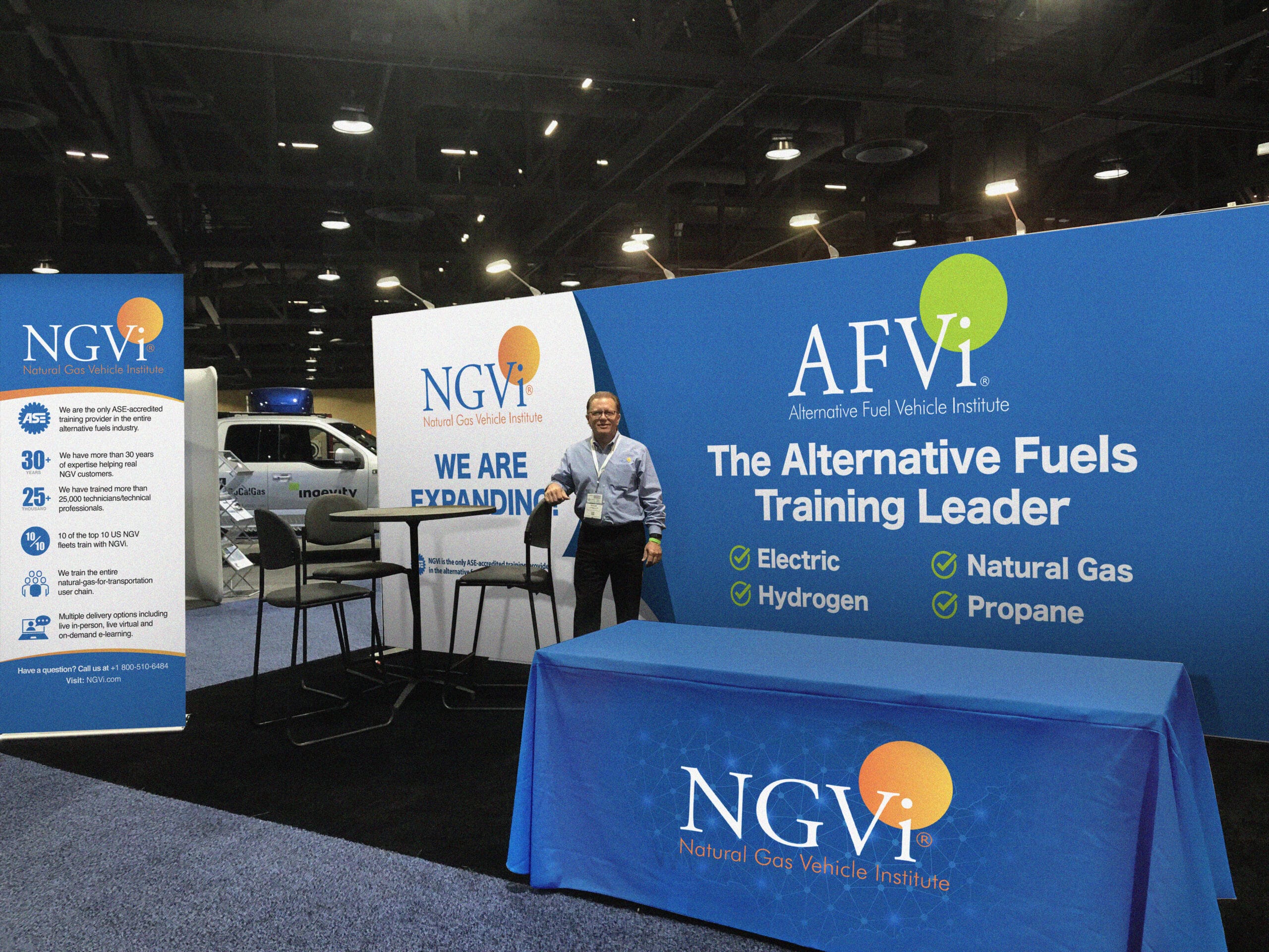 An NGVi employee stands at their ACT booth while display boards announce AFVi, the Alternative Fuel Vehicle Institute.